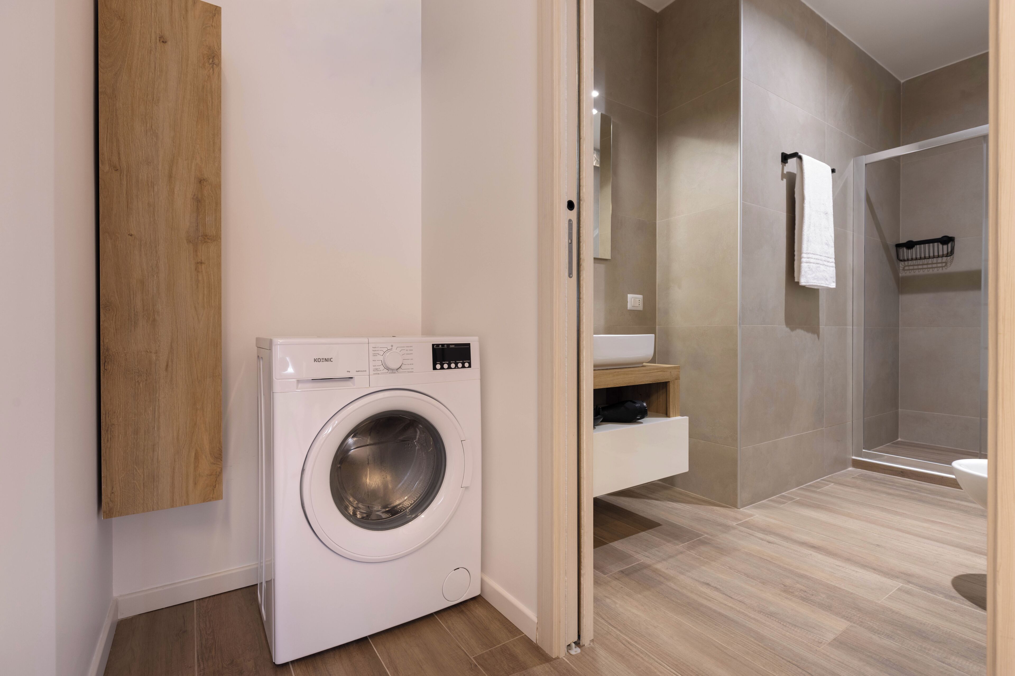 Une salle de bain moderne dotée d’un lave-linge encastré, d’un espace douche et d’un plancher en bois.