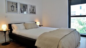 Ett sovrum med en säng, två sänglampor, ett fönster med utsikt och tre inramade tavlor på väggen.