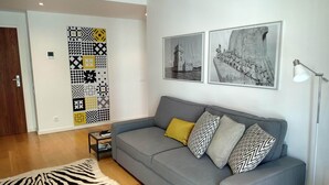 Ett vardagsrum med en grå soffa, mönstrade kuddar, en matta med zebraströmmar och två svartvita fotografier på väggen.