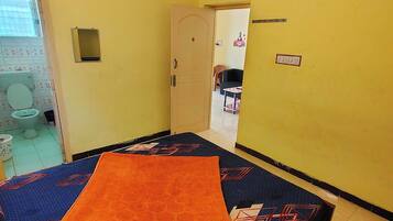 A room with a bed, a door leading to a bathroom, and a small table with a chair.