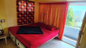 A bedroom with a bed, a ceiling fan, a window with curtains, and a wall with a patterned tapestry.