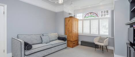 A room with a grey sofa, a wooden cabinet, a radiator, and a chair.