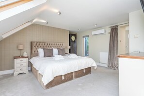A bedroom with a large bed, a bedside table, a lamp, a clock, an air conditioning unit, and a window with curtains. - Large 3BDR Wimbledon House with Garden and Office (Greater London)