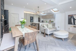 A modern kitchen with built-in appliances, a dining area with a wooden table and chairs, and a living area with a sofa and ottoman. - Large 3BDR Wimbledon House with Garden and Office (Greater London)