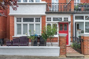 A row of terraced houses with white and red facades, a small garden, and a metal fence. - Large 3BDR Wimbledon House with Garden and Office (Greater London)