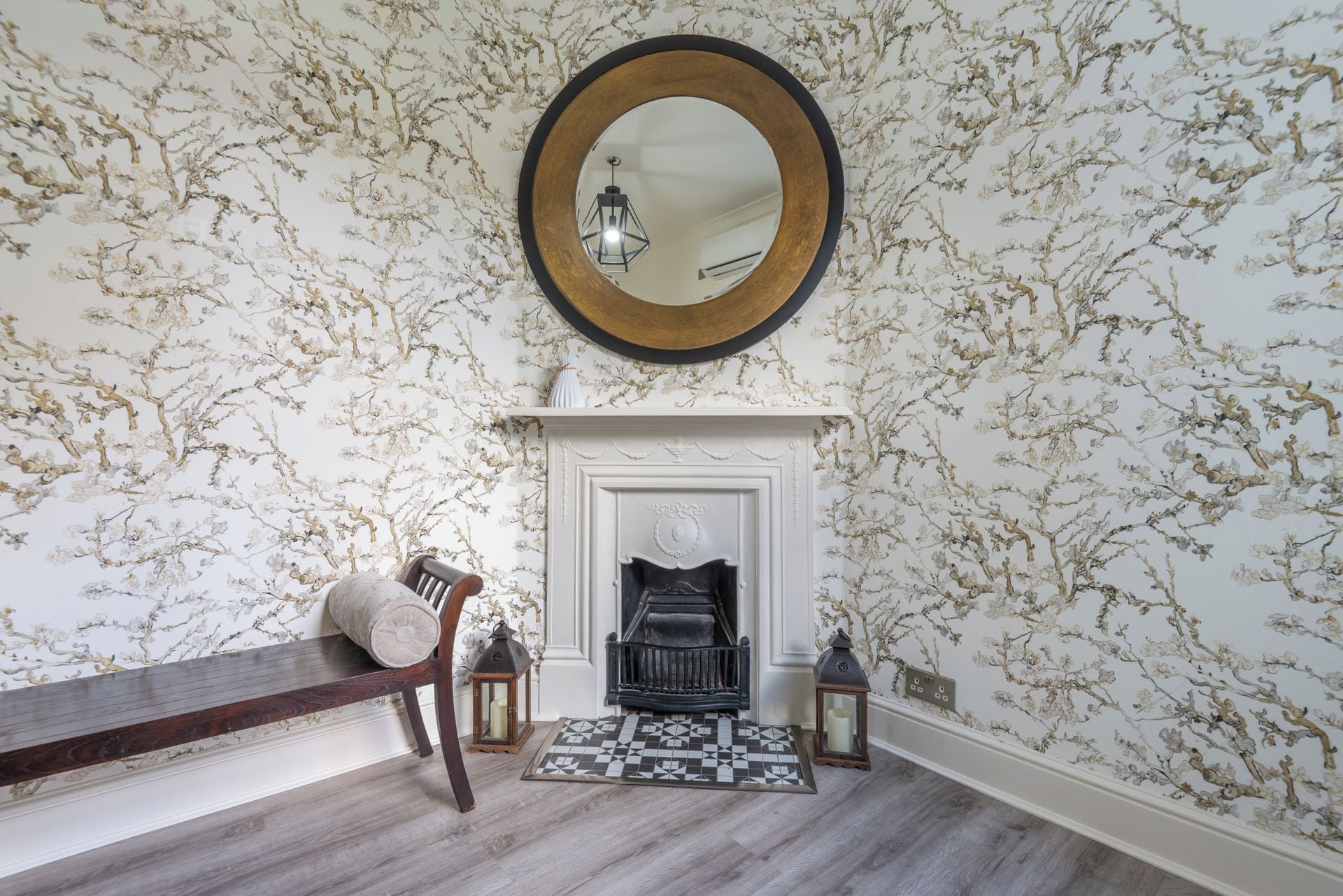A room with a fireplace, a round mirror, and patterned wallpaper.