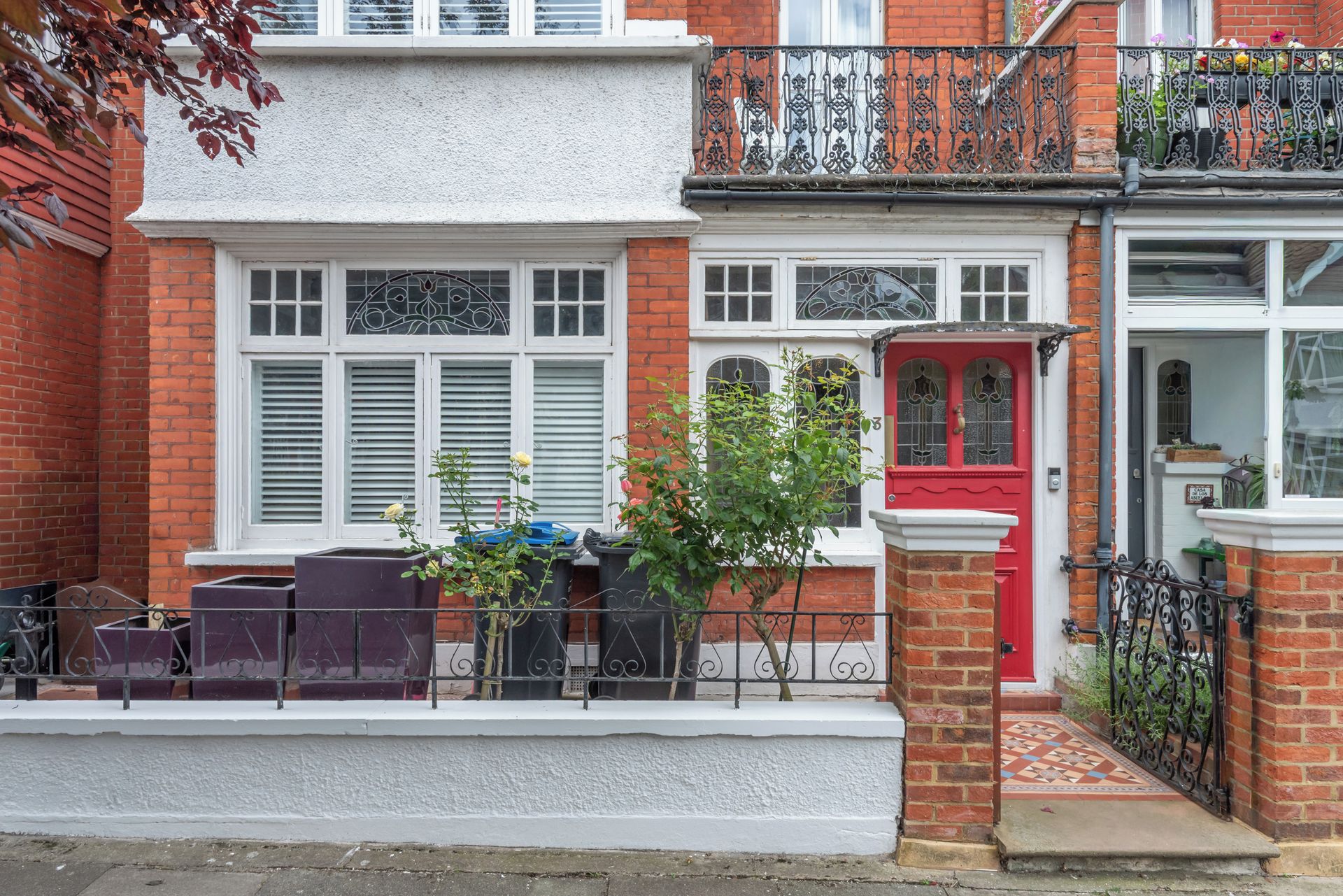 A row of terraced houses with white and red facades, a small garden, and a metal fence.