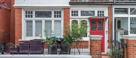 A row of terraced houses with white and red facades, a small garden, and a metal fence.