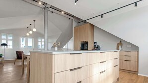 A modern kitchen with a central island, wooden cabinets, and a dining area with a chair and table. - Amtmann Residence - Four Bedroom Penthouse (Selfoss)