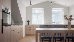 A modern kitchen with wooden cabinets, a central island with chairs, and large windows. - Amtmann Residence - Four Bedroom Penthouse (Selfoss)