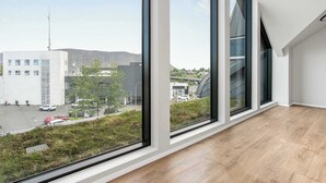 A room with large windows, a wooden floor, and a view of a building with a modern design. - Amtmann Residence - Four Bedroom Penthouse (Selfoss)