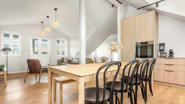 A modern kitchen with wooden cabinets, a dining table with chairs, and a coffee machine. - Amtmann Residence - Four Bedroom Penthouse (Selfoss)