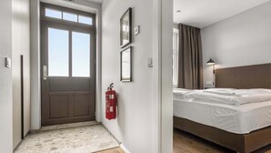 Habitació d'hotel amb un llit, un extintor i una porta amb finestral.