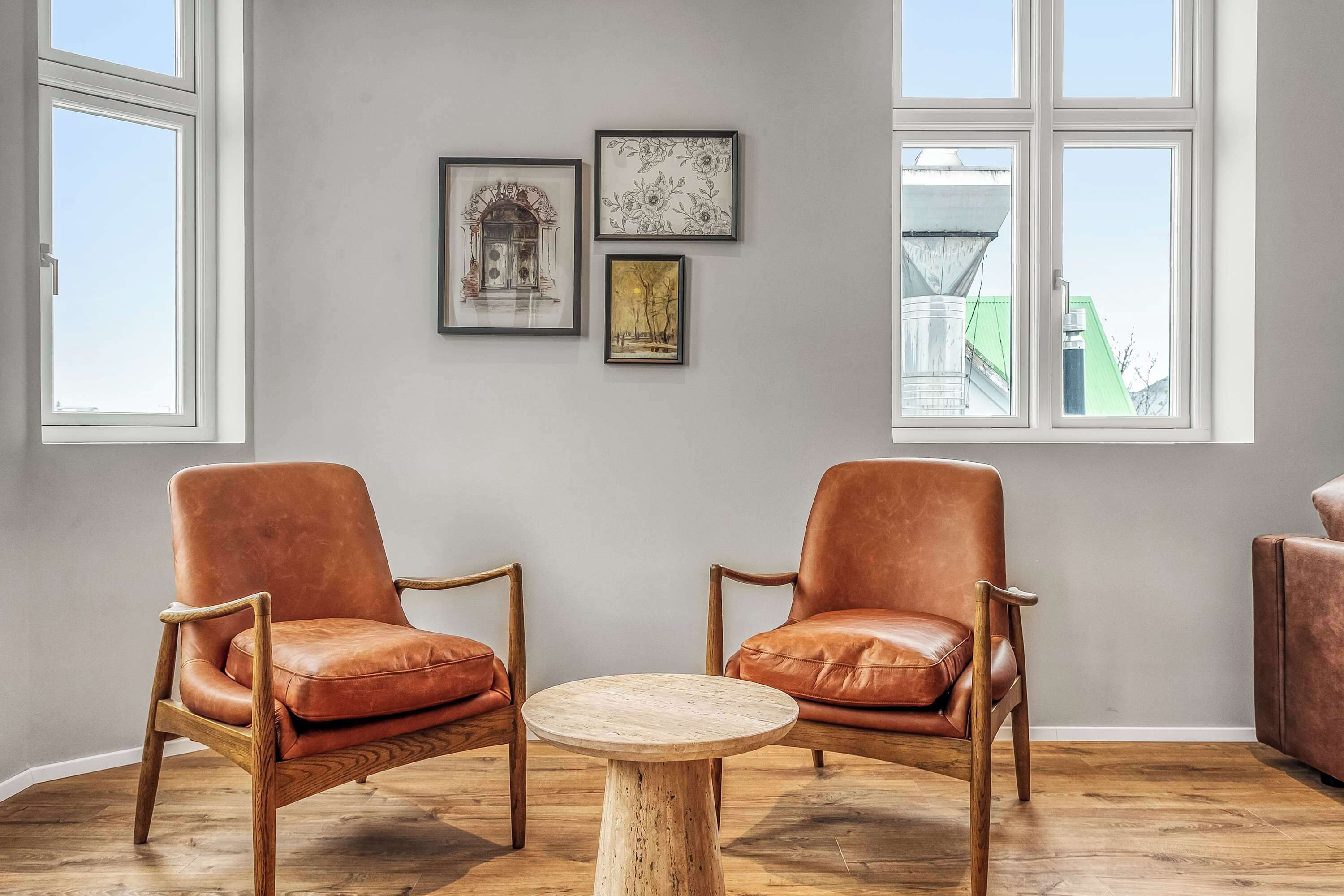 Um quarto com duas poltronas de couro, uma mesa de madeira redonda e três obras de arte emolduradas na parede.