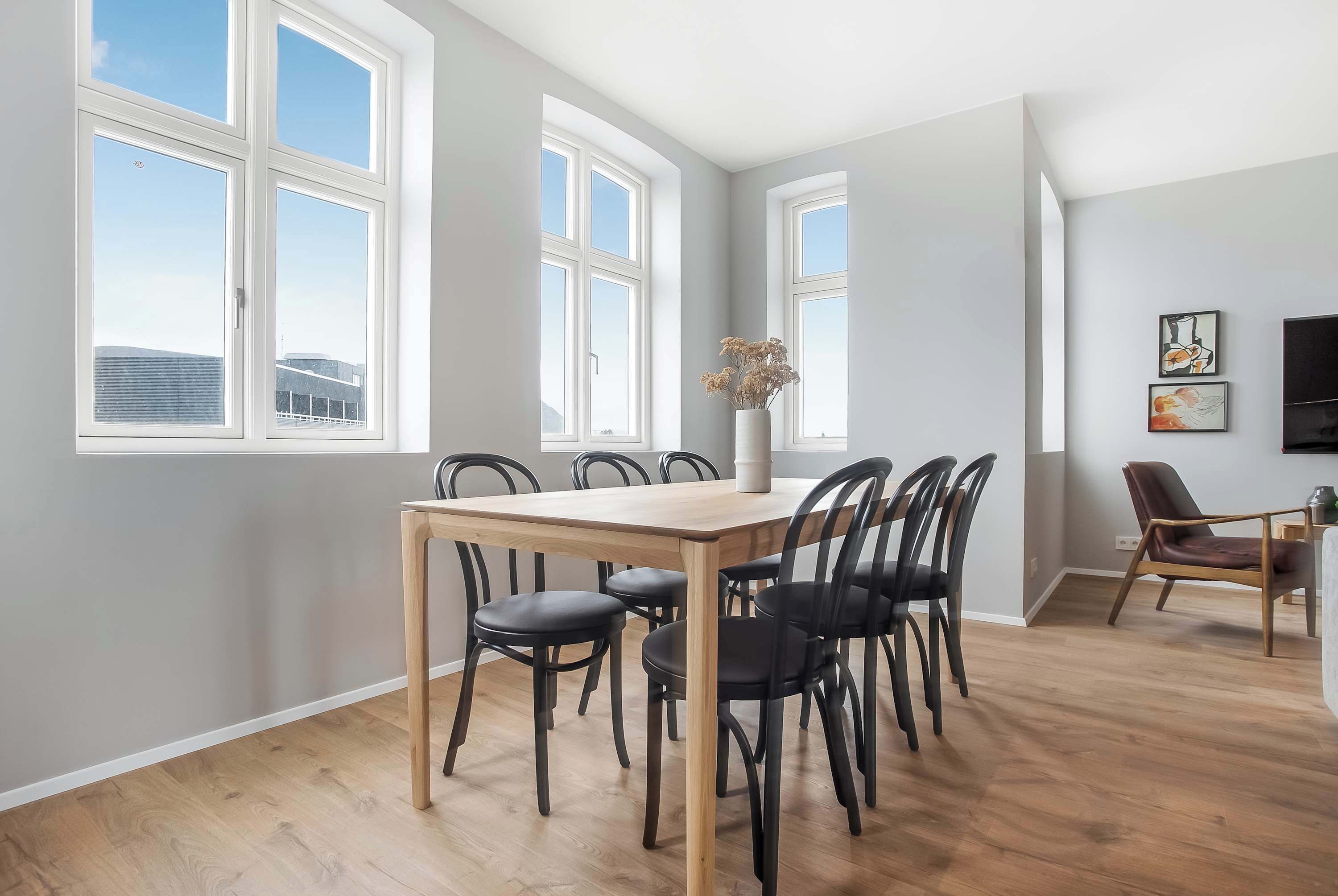 A dining area with a wooden table and black chairs, large windows, and a view of buildings outside.