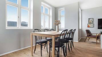 A dining area with a wooden table and black chairs, large windows, and a view of buildings outside.