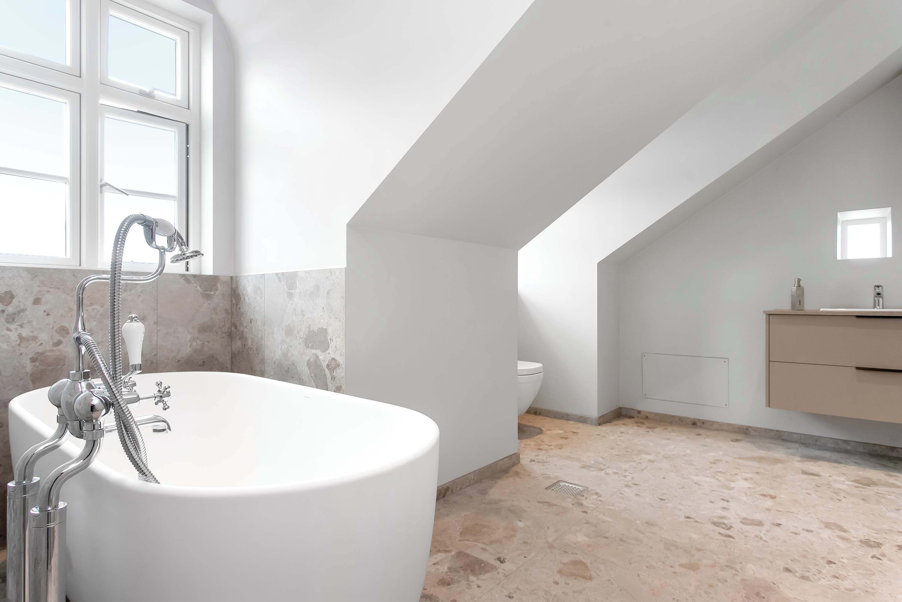 Ein modernes Badezimmer mit einer freistehenden Badewanne, einer Toilette und einem Fenster.