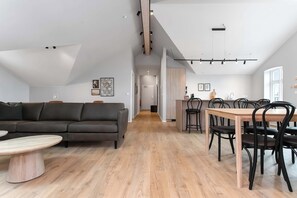 A modern interior with a sofa, dining table, and chairs, a kitchen area, and a hallway leading to another room. - Amtmann Residence - Three Bedroom Penthouse (Selfoss)