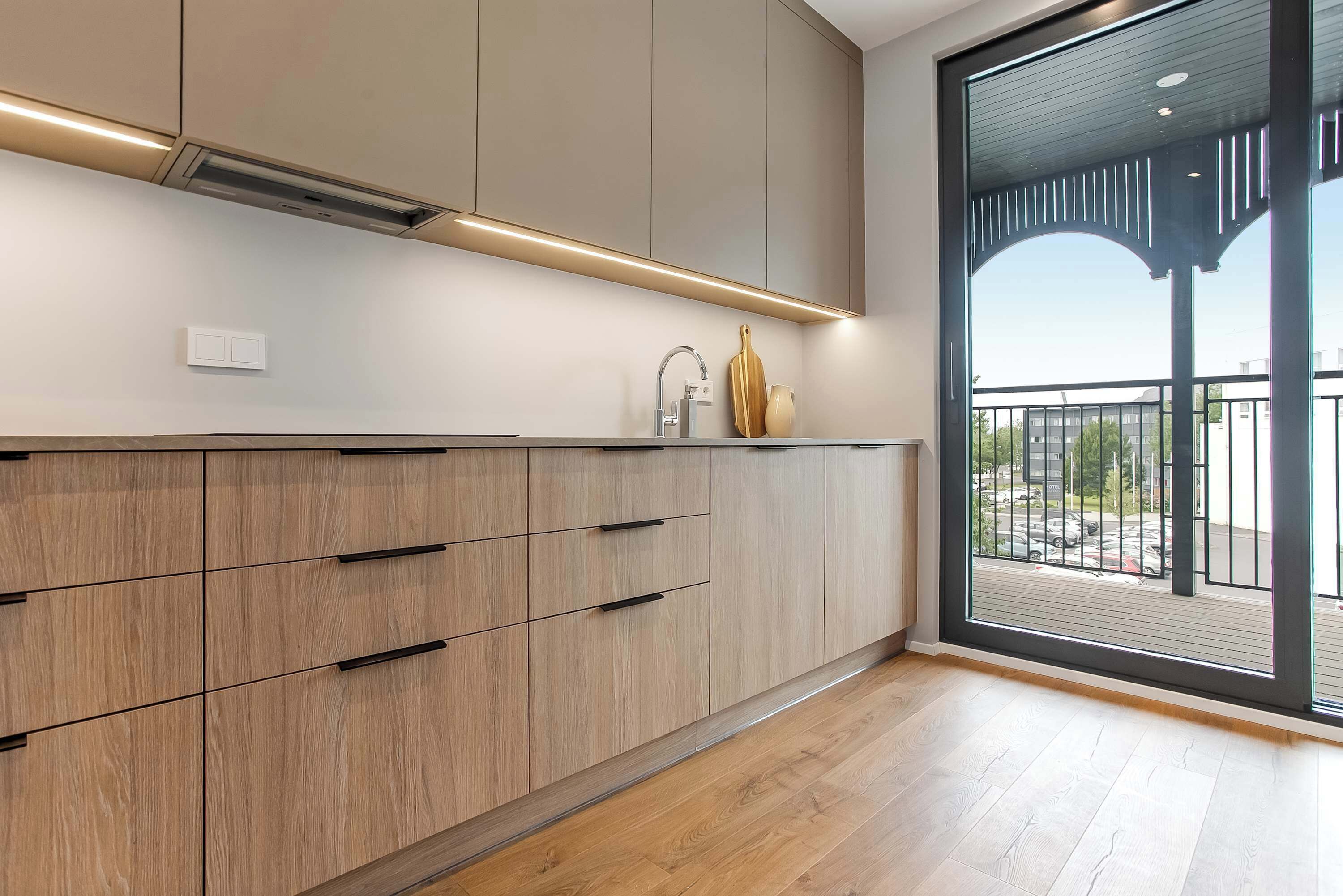 A modern kitchen with wooden cabinets, a built-in oven, and a large window overlooking a balcony.