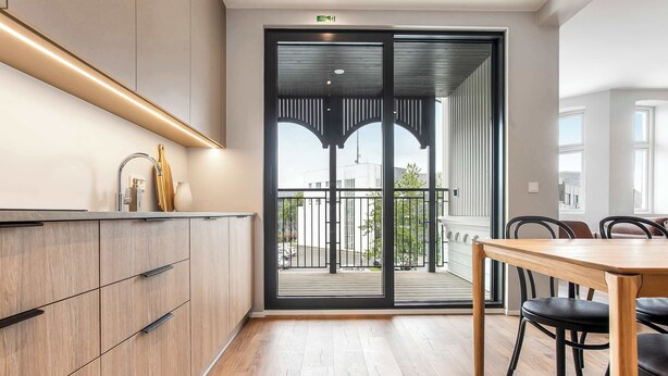 A modern kitchen with a wooden countertop and cabinets, a dining area with a wooden table and chairs, and a sliding glass door leading to a balcony with a view of the city.