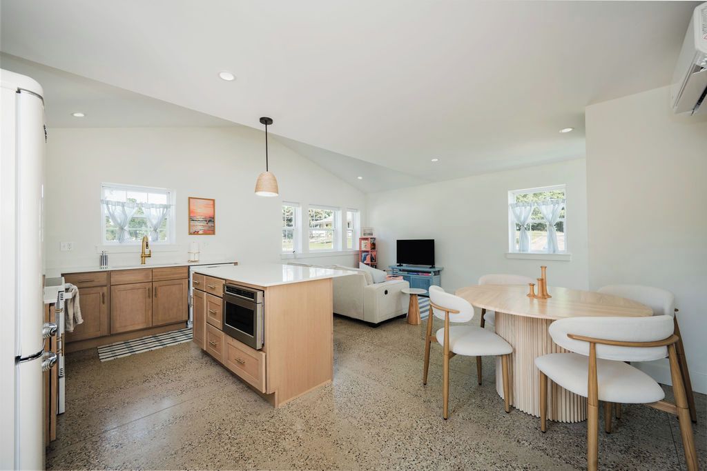 A modern kitchen with a central island, a dining area with a round table and chairs, and a living space with a sofa and television.