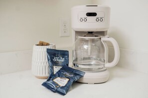 Màquina de cafè blanca amb pantalla digital, un decantador de vidre transparent i dues càpsules de cafè sobre una superfície de cuina blanca.
