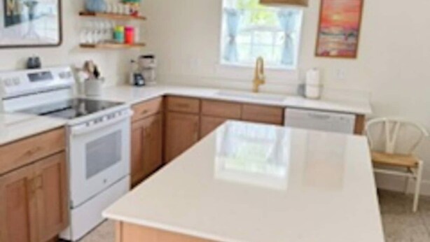 Een keuken met een centraal eiland, houten kastjes, een witte kookplaat en een hangende lamp.