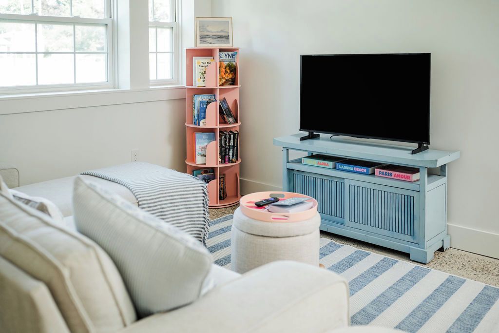 Un salon avec un canapé, un pouf et un téléviseur posé sur un meuble.