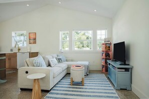 A living room with a sofa, ottoman, and a television on a stand.