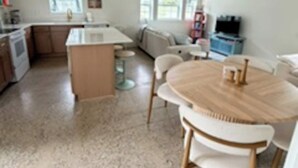Een moderne keuken met granieten aanrecht, een eethoek met een ronde houten tafel en witte stoelen, en een zithoek met een bank en een televisie.