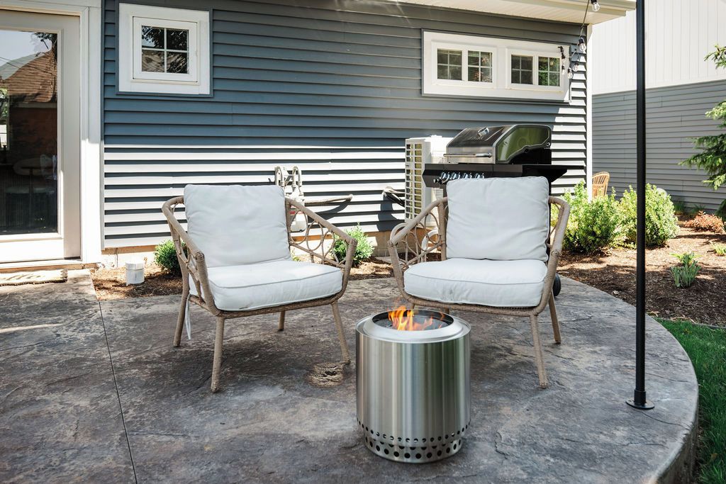 A patio with two wicker chairs and a metal fire pit.