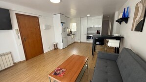 A modern kitchen with white cabinets, a wooden dining table, and a gray sofa. - Ramon Apartment (Tarragona)