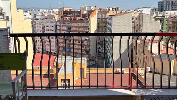 A balcony with a view of a cityscape, a tiled floor, and a metal railing. - Ramon Apartment (Tarragona)