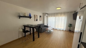 A modern living room with a dining area, a sofa, a small table, and a kitchen area with a refrigerator. - Ramon Apartment (Tarragona)