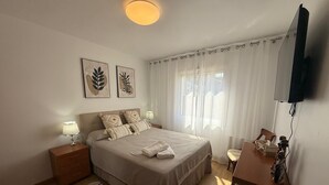 A bedroom with a bed, bedside lamps, a desk, a chair, a television, and artwork on the wall. - Ramon Apartment (Tarragona)