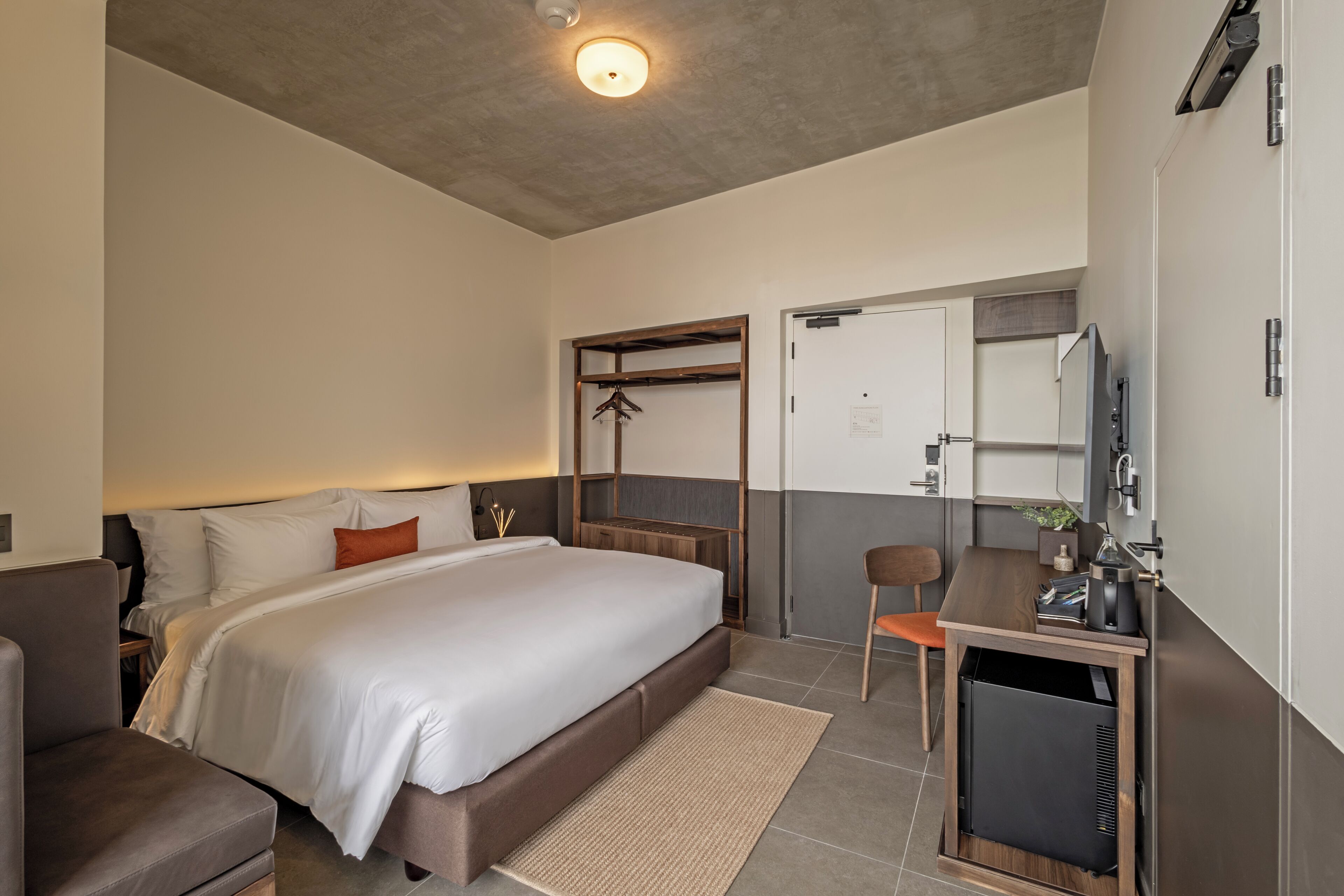 A modern hotel room with a bed, a desk, a chair, a wardrobe, and a television.