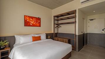 A hotel room with a bed, a wall-mounted artwork, a wooden shelf with clothes, and a door leading to another room.