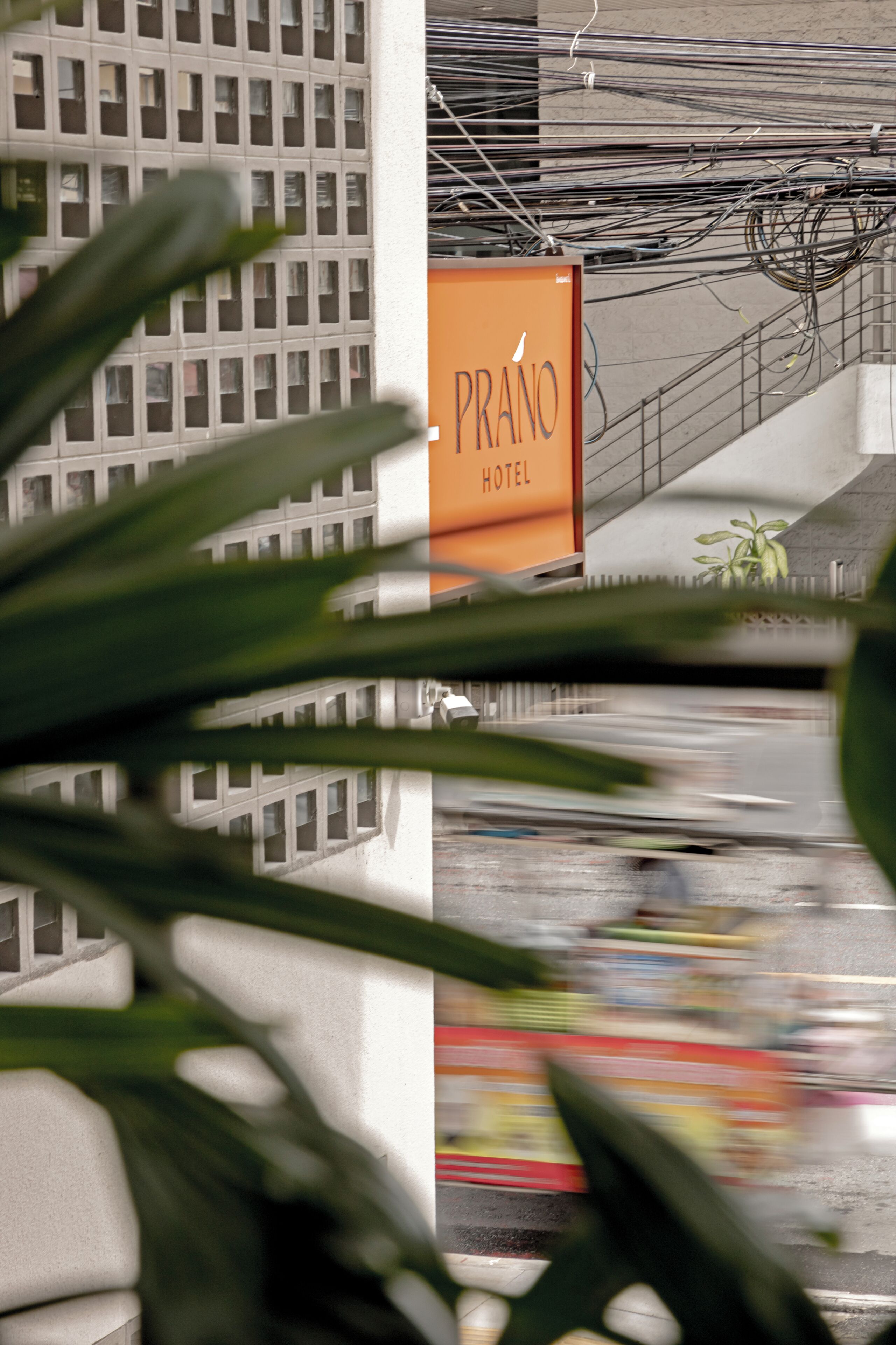 A hotel sign with the name 'PRANO HOTEL' and a view of a building with a grid-like facade.