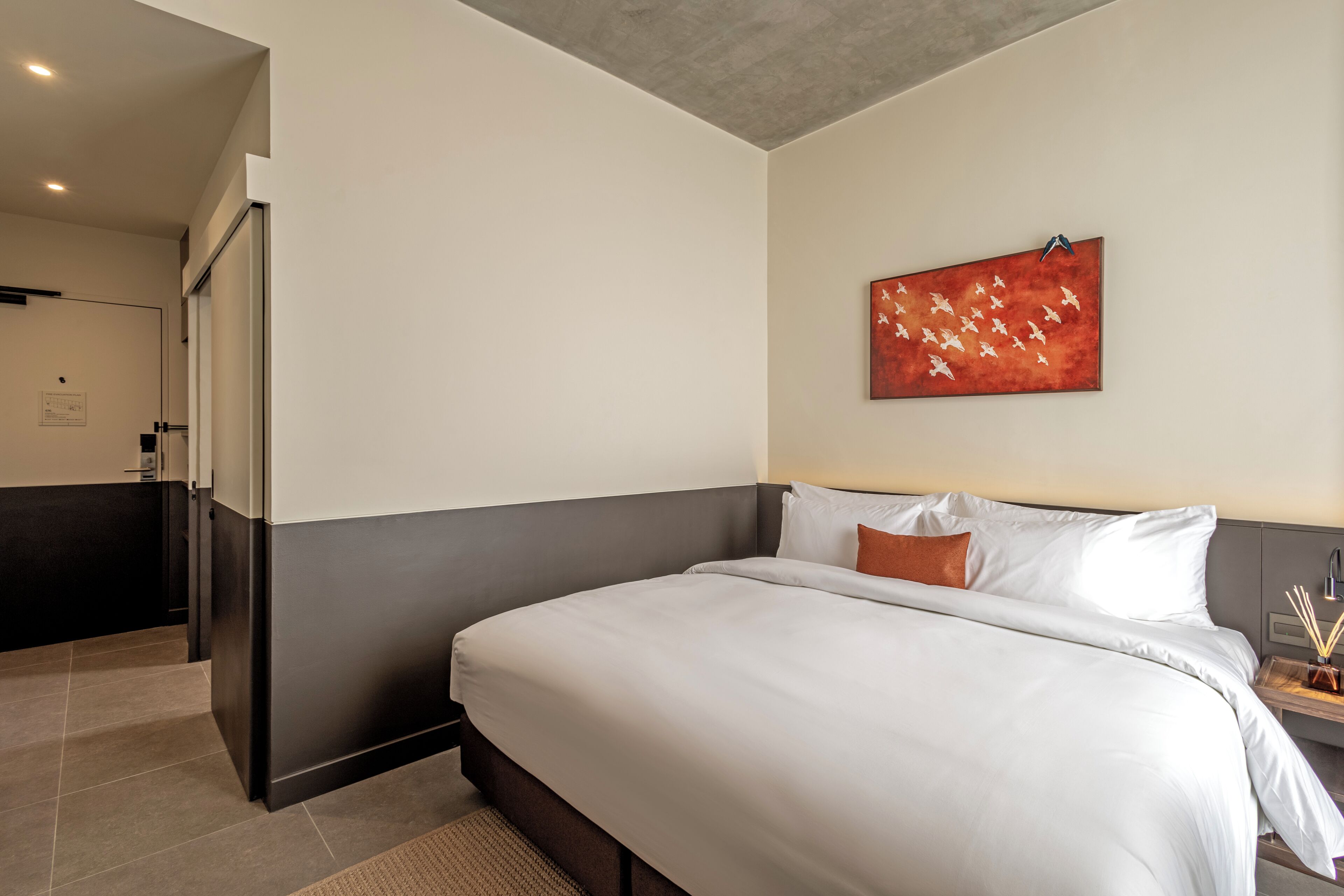 Una habitación de hotel moderna con una cama grande, una mesita de noche pequeña y un cuadro en la pared.