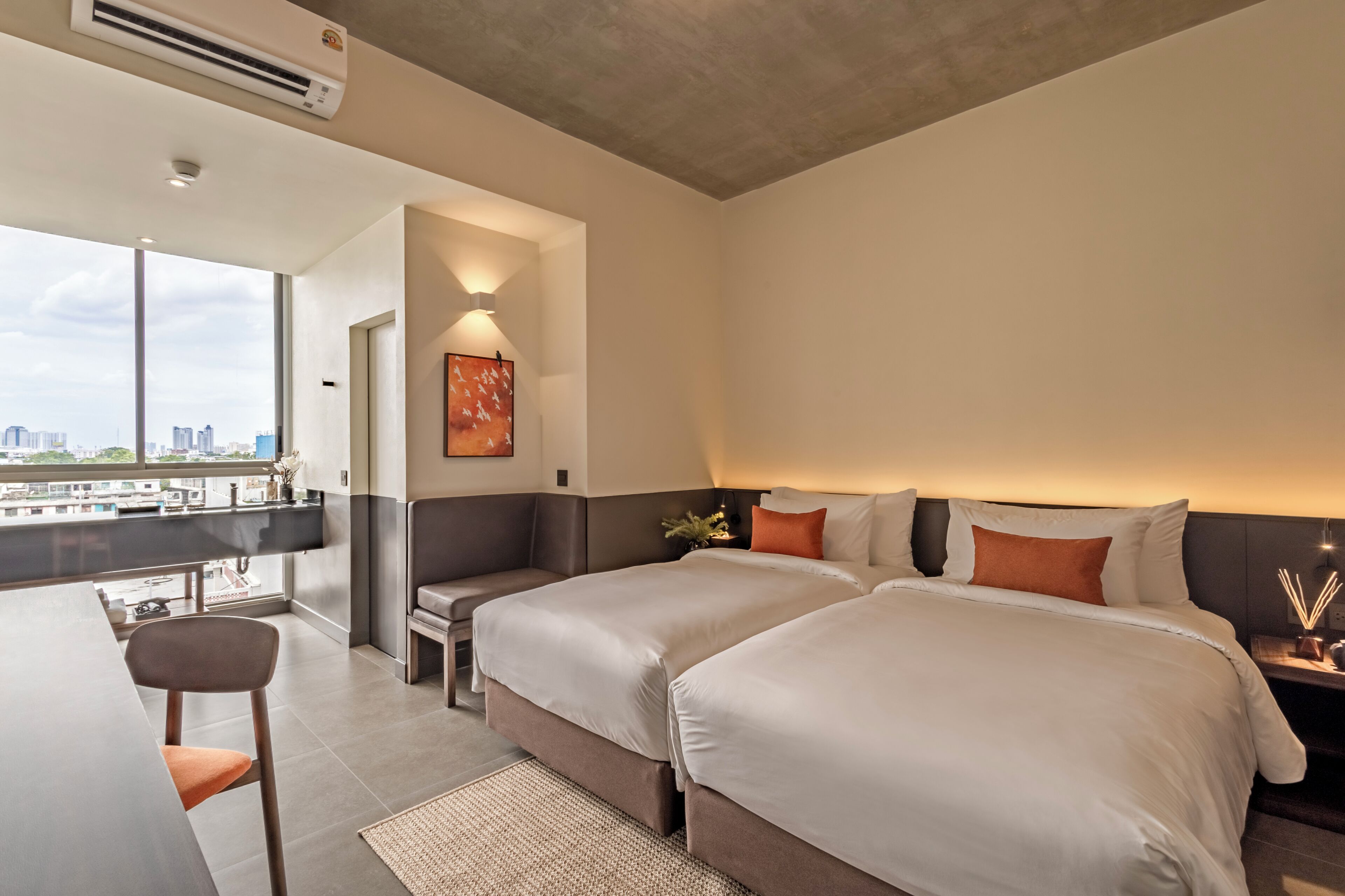 A hotel room with two beds, a desk, and a view of the city.