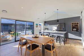 Una cucina moderna con isola centrale, zona pranzo con arredi in legno e un'ampia porta scorrevole in vetro che dà su un patio esterno.