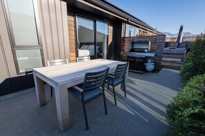 Una terrazza esterna con tavolo e sedie di legno, una porta scorrevole in vetro che dà su una camera da letto e un barbecue.