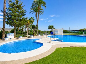 Ein Swimmingpool mit einer umlaufenden Liegefläche, Palmen und blauem Himmel.