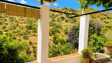 A balcony with a view of a hilly landscape, white pillars, and potted plants.