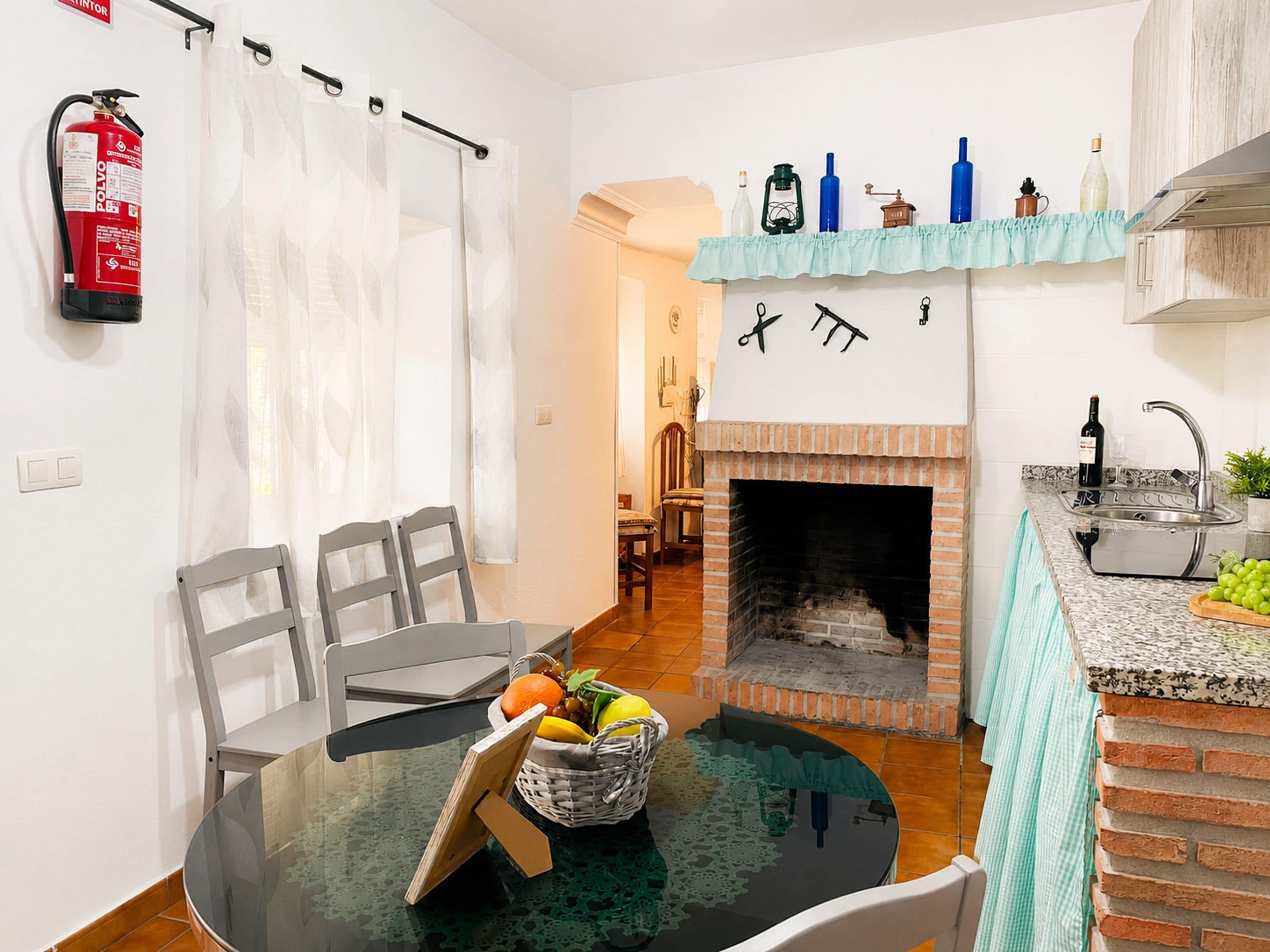A compact kitchen with a fireplace, a dining area with chairs and a table, and a small bar area with a sink and countertop.