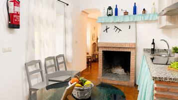 A compact kitchen with a fireplace, a dining area with chairs and a table, and a small bar area with a sink and countertop.