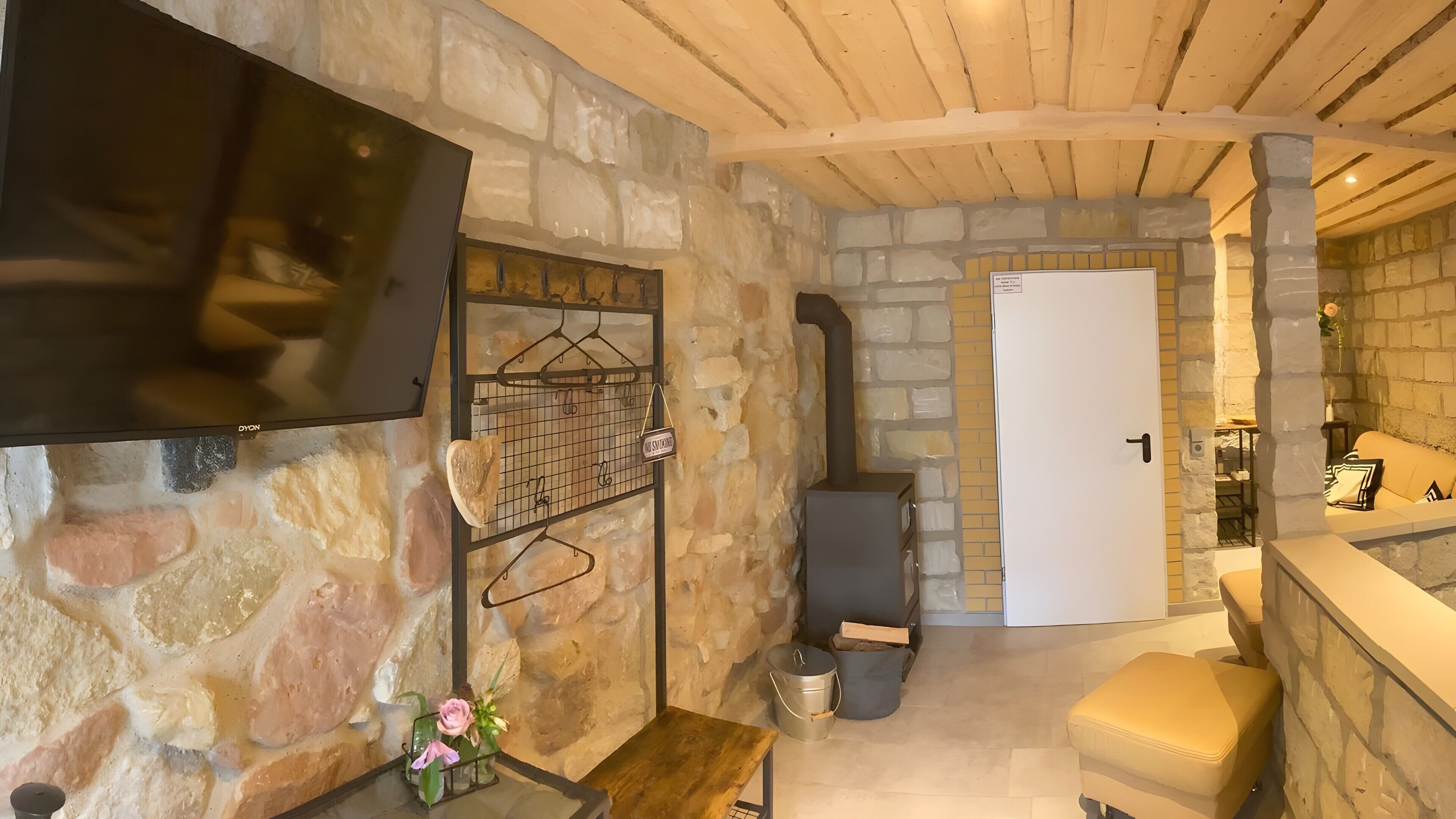 A stone-walled room with a fireplace, a television mounted on the wall, and a door leading to another room.