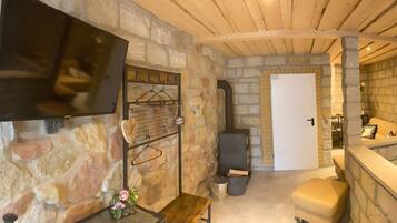 A stone-walled room with a fireplace, a television mounted on the wall, and a door leading to another room.