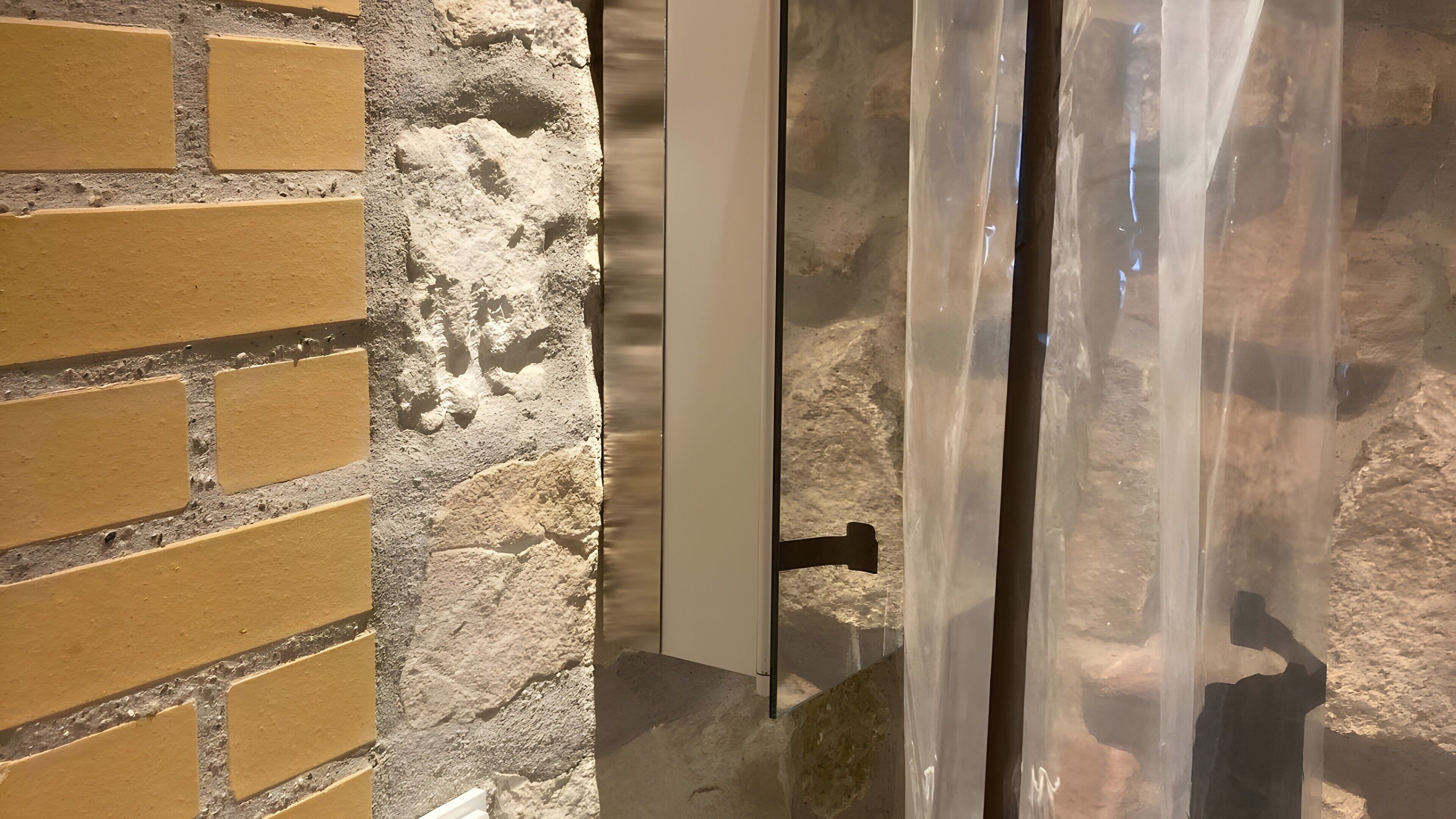 Un mur de briques, un mur de pierres brutes et une porte en verre avec une poignée en métal.
