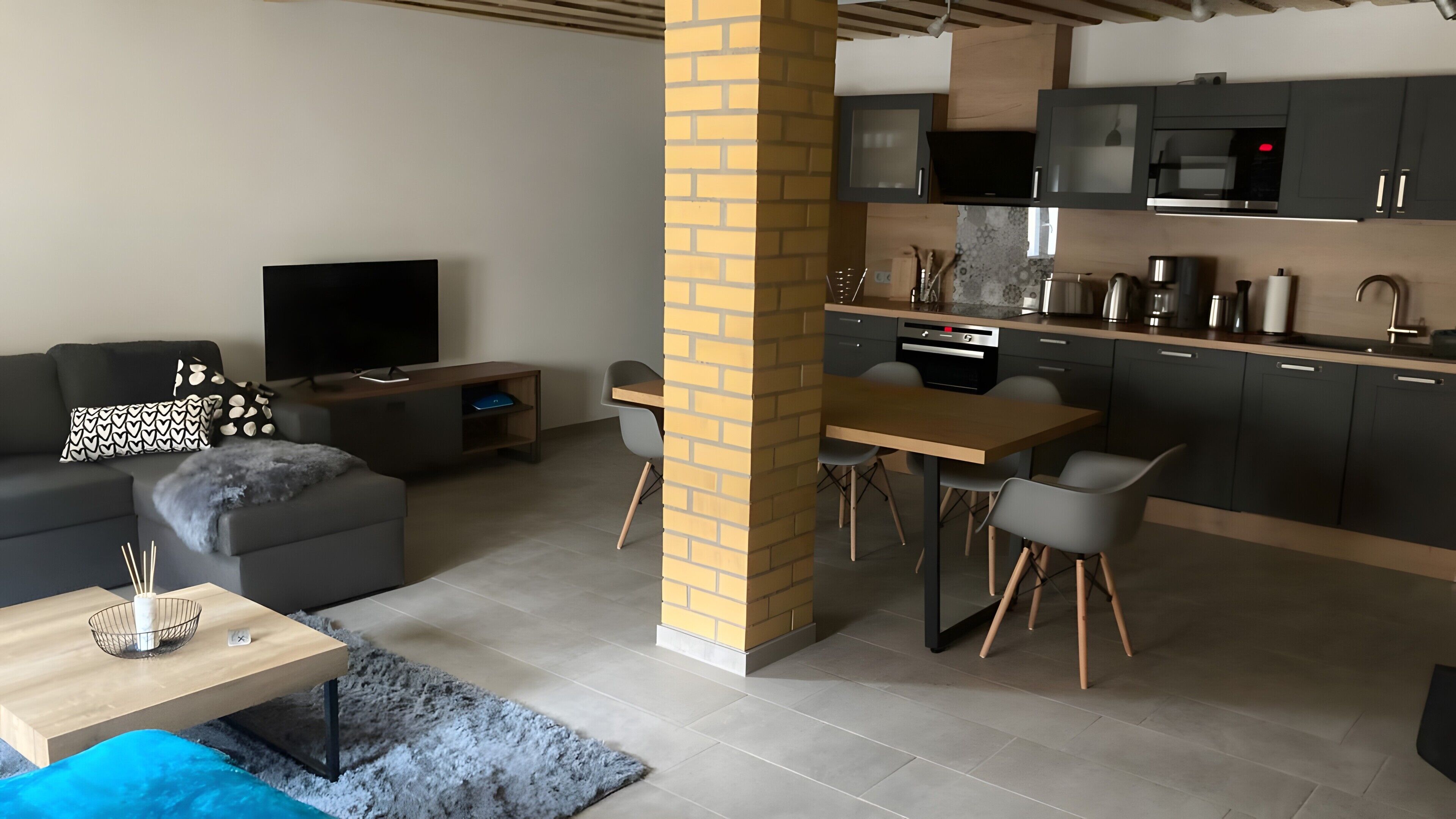 Una sala de estar moderna con un sofá, televisión y un comedor con sillas y una mesa.
